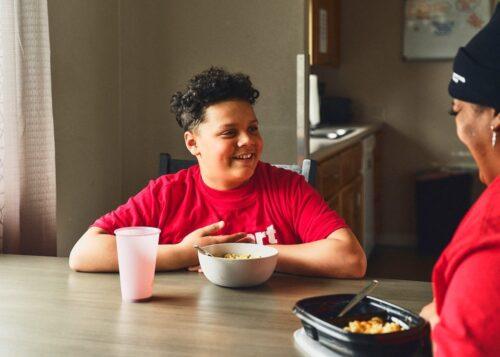 A boy with developmental disabilities shares a meal with a direct support professional at a residence.