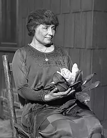 Black-and-white portrait of Helen Keller sitting in a chair holding flowers circa 1920. 