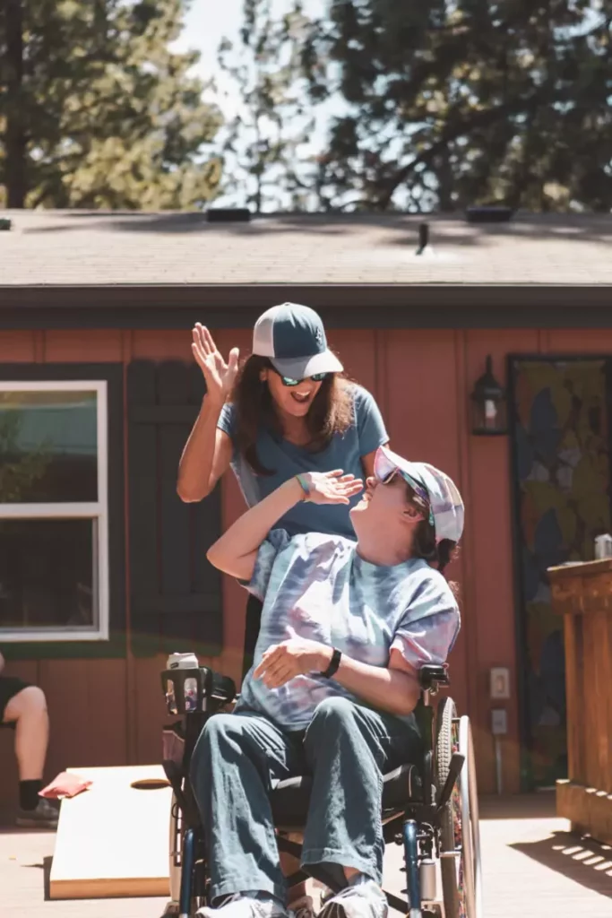 A DSP worker high fives a developmentally disabled man in a wheelchair on the deck of a home. 