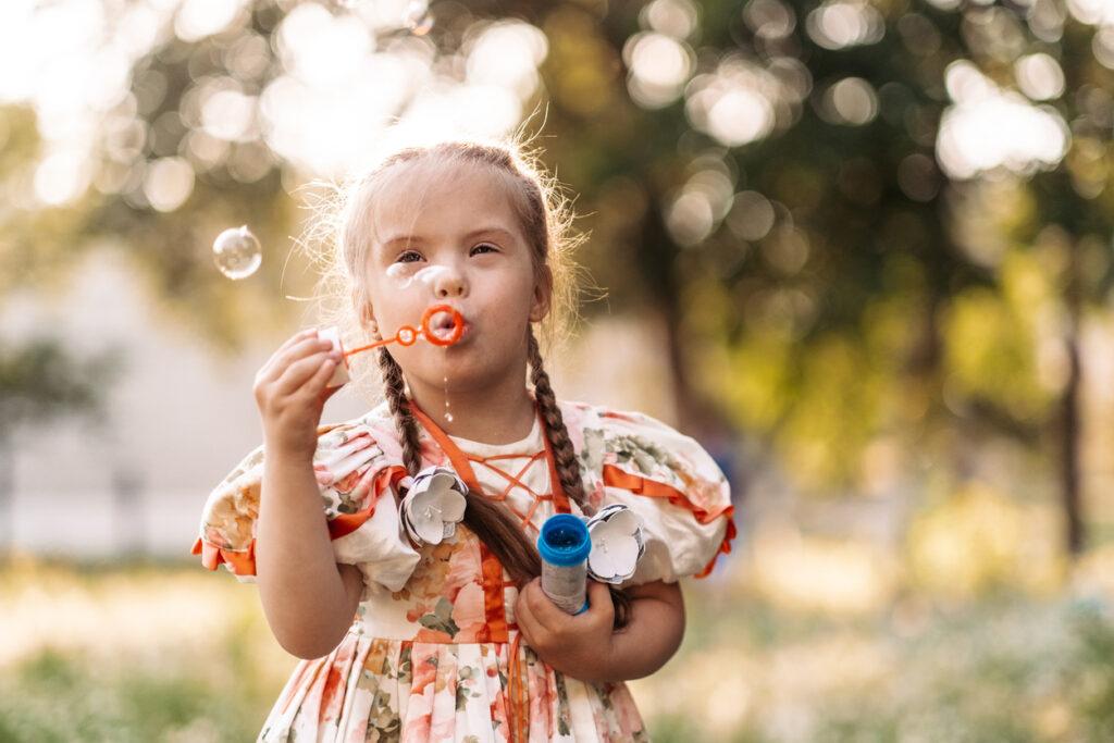 A girl with Down Syndrome blowing bubbles outdoors. 