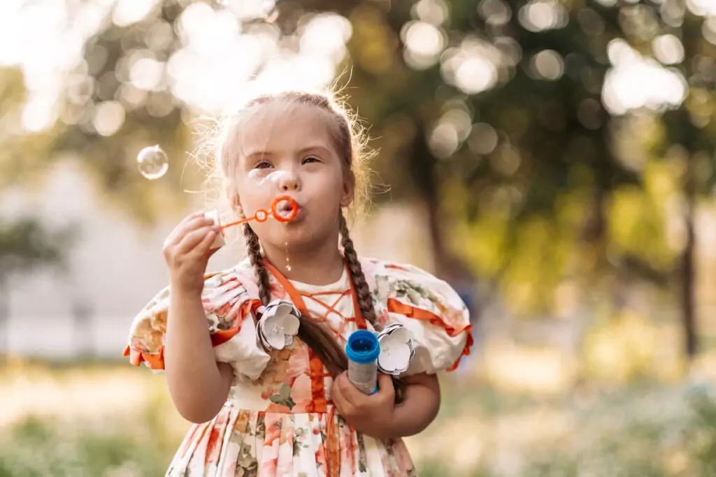 A girl with Down Syndrome blowing bubbles outdoors. 