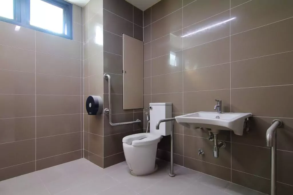 An office restroom design for the disabled with grab bars next to the toilet as well as on each side of the sink. 