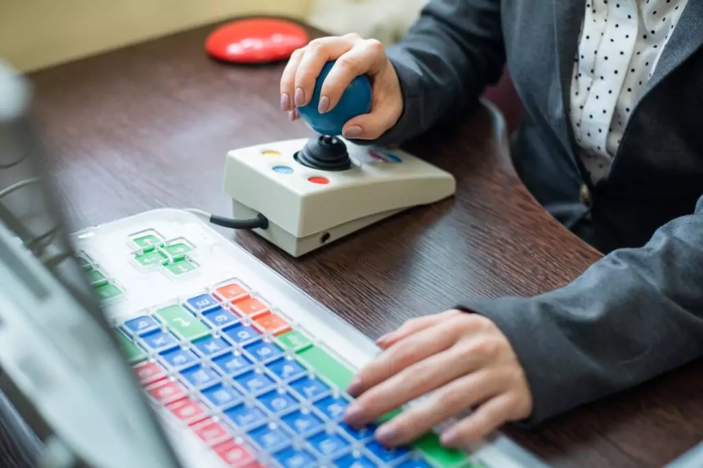 Close up of a woman with cerebal palsy using assistive technology on a computer including a joystick in place of a mouse.