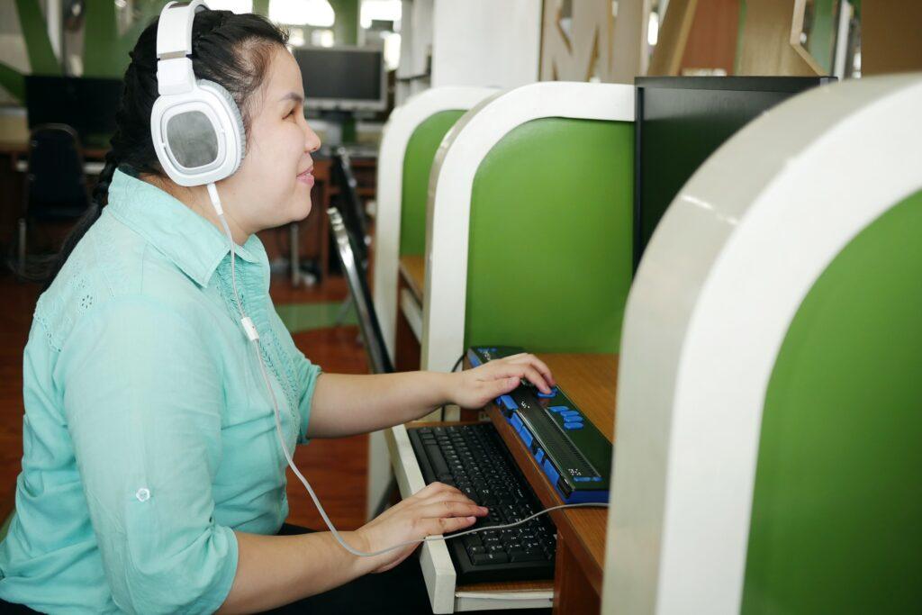 A visually impaired woman at work on a computer with assistive technology including a headphone and special keyboard. 