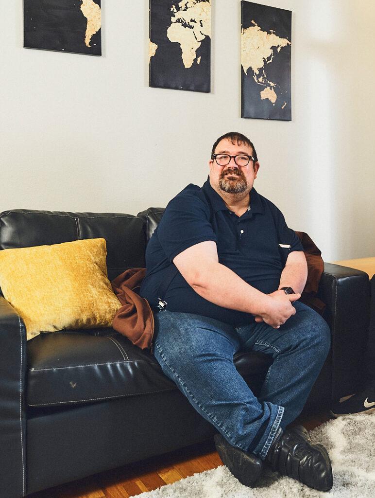 Joe, a person with disabilities that ALSO supports, sits on a couch.