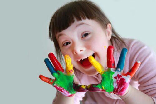 Girl with Down's Syndrome smiling and showing the different paint colors on her hands.