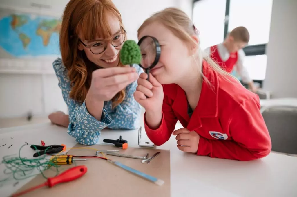 A teacher works with a developmentally disabled girl who is looking through a magnifying glass at an object.