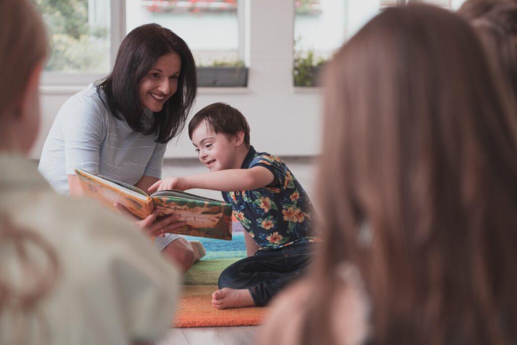 A female teacher reading to a boy with Down's Syndrome. 