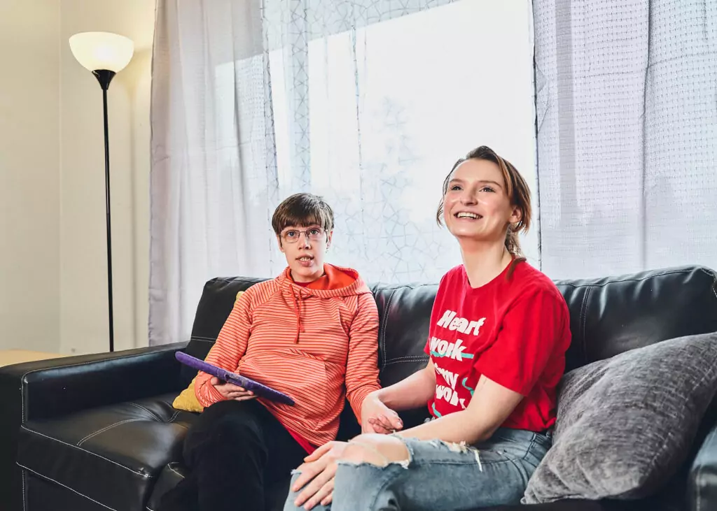 An ALSO direct support professional sits on a sofa talking with a developmentally disabled client.