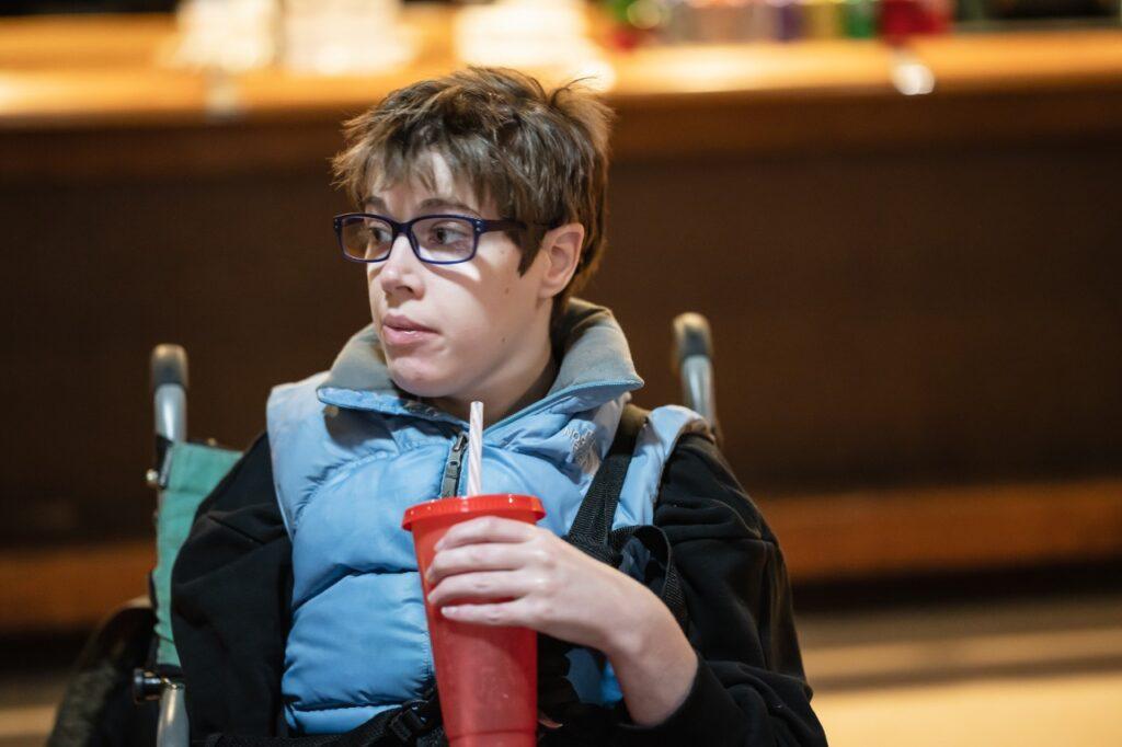 A developmentally disabled woman sits in a wheelchair with a beverage at the ALSO holiday party in Portland, Oregon.