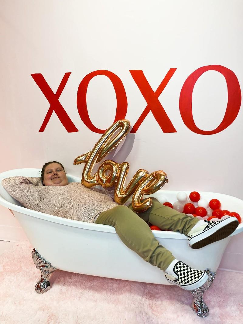 A developmentally disabled woman lies in bathtub with an "XOXO" sign above as part of an event.