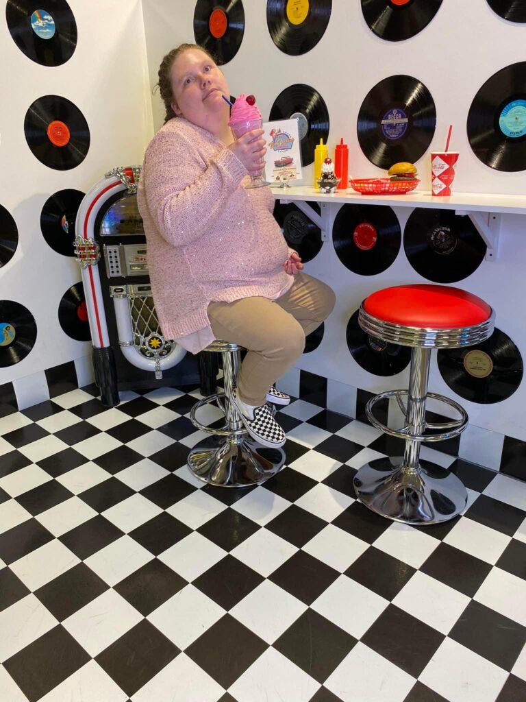 A developmentally disabled woman sits in a retro diner holding an ice cream cone. 