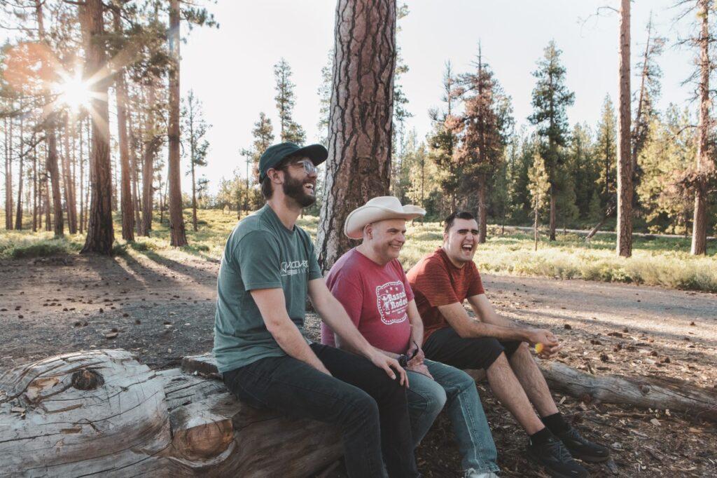 A direct support professional sits with two intellectually disabled individuals and rests during a hike on a trail in Oregon. 