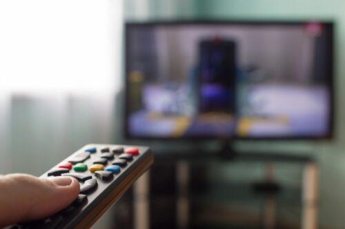 Close up of a man's hand pointing a remote control at the tv.