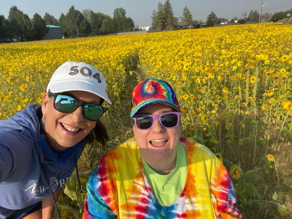 An ALSO direct support professional with her disabled client posing for the camera in a field of wildflowers.