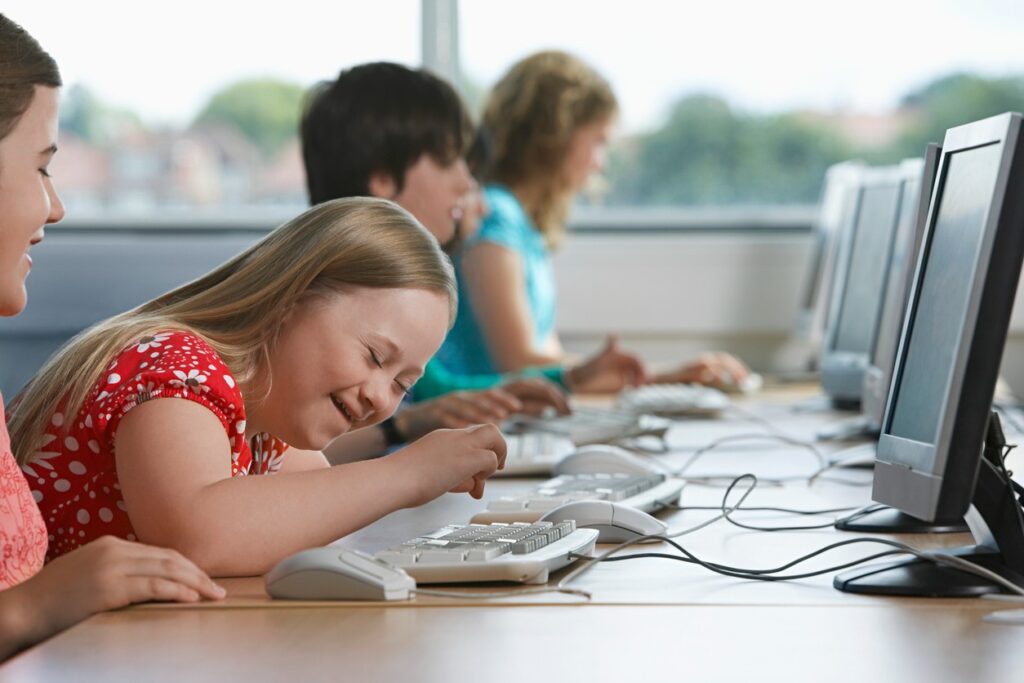 A young girl with assistive technology works on a computer in the classroom.
