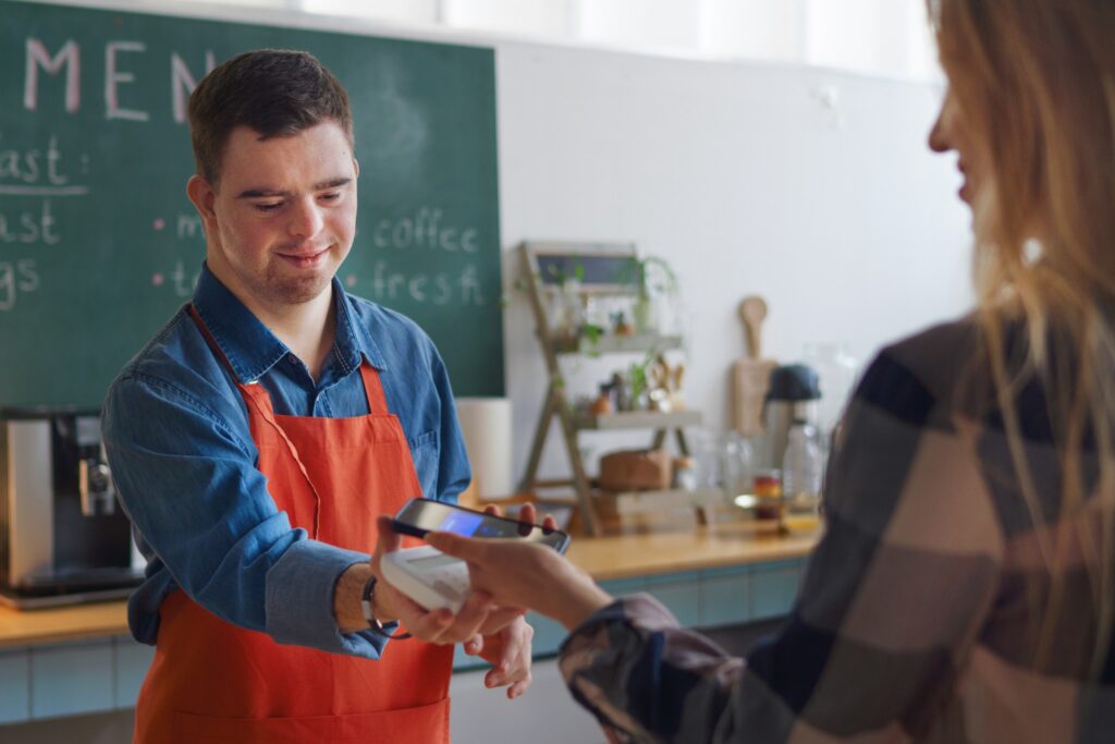 A teen male with Down Syndrome works at a coffee shop. 