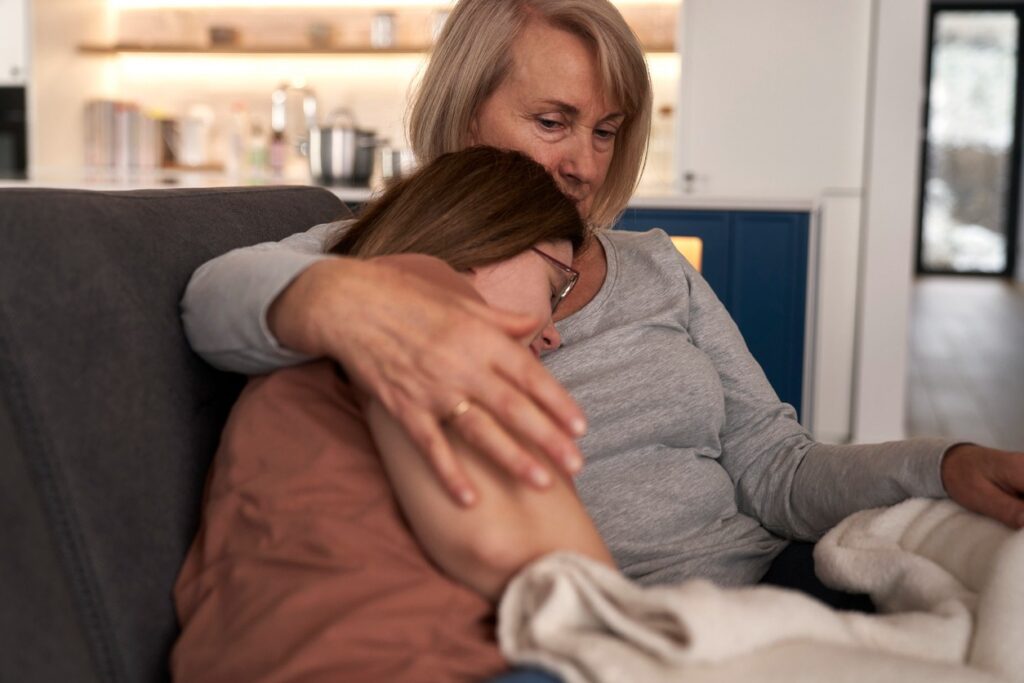 A mother hugs and comforts her developmentally disabled daughter while sitting on a sofa.