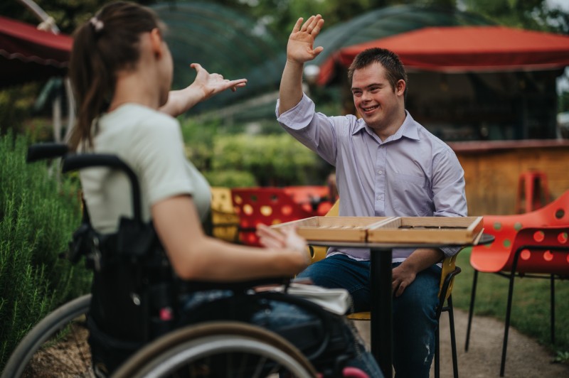 A young man with I/DD high fives a friend in a wheel chair.