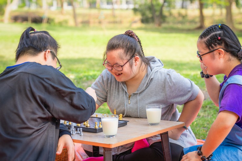 Three young women with I/DD play chess together outside. 